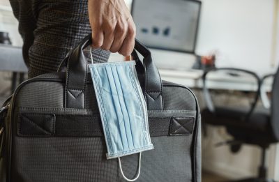 closeup of a young man in an office holding a briefcase and a surgical mask in his hand